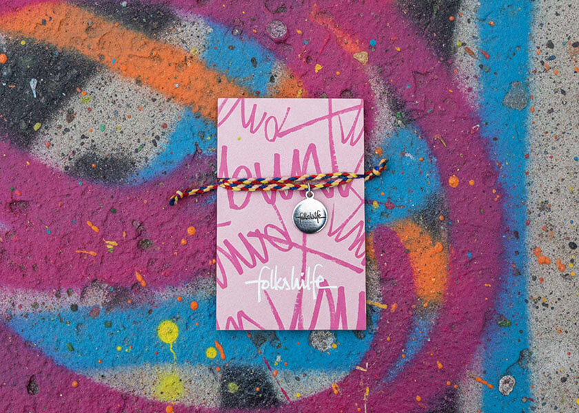 Pinkes geflochtenes Freundschaftsarmband mit Logo-Charm auf bedruckter Karte als individuelles Giveaway