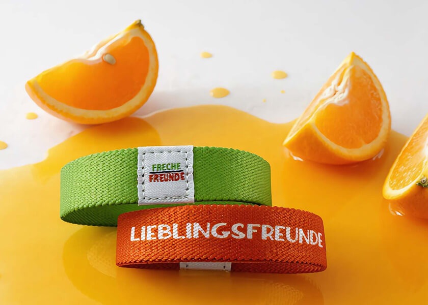 Oranges flexibles Wendearmband mit wiederholtem Schriftzug als individuell bedrucktes Promoarmband